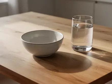Ein schlichter Holztisch mit einer leeren Keramikschale und einem Glas Wasser in natürlichem Licht. - Foto: über boerse-global.de