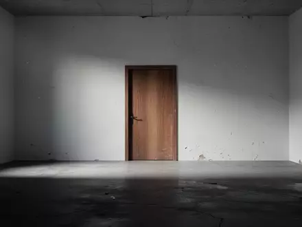 Eine leere, minimalistische Räumlichkeit mit einer geschlossenen Holztür und langen Schatten auf einem Betonboden. - Foto: über boerse-global.de