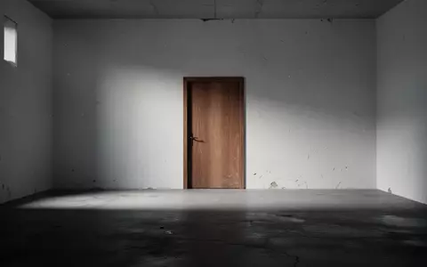 Eine leere, minimalistische Räumlichkeit mit einer geschlossenen Holztür und langen Schatten auf einem Betonboden. - Foto: über boerse-global.de