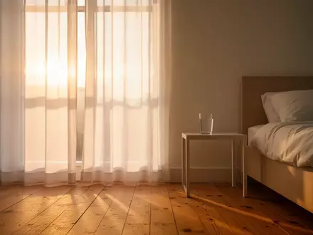 Ein helles, minimalistisches Schlafzimmer bei Sonnenaufgang mit einem Glas Wasser auf dem Nachttisch. - Foto: über boerse-global.de