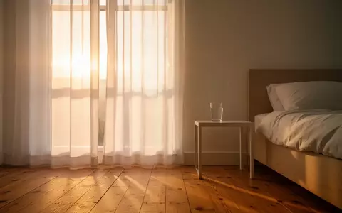 Ein helles, minimalistisches Schlafzimmer bei Sonnenaufgang mit einem Glas Wasser auf dem Nachttisch. - Foto: über boerse-global.de
