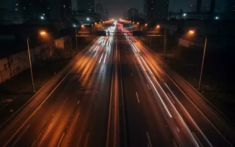 Eine nächtliche, schwach beleuchtete Autobahn in einer städtischen Umgebung mit verschwommenen Lichtspuren des Verkehrs. - Foto: über boerse-global.de