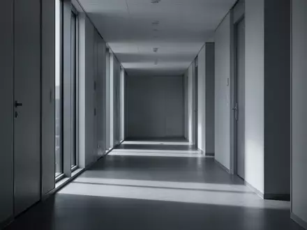 Ein leerer, minimalistischer Flur in einem modernen Bürogebäude mit langen Schatten und kühlem Tageslicht. - Foto: über boerse-global.de