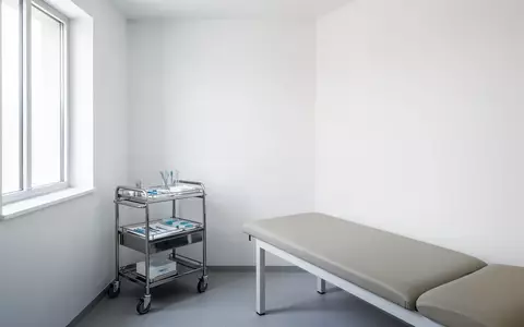 Ein steriler, minimalistischer Behandlungsraum in einer Arztpraxis mit einem Untersuchungstisch und einer medizinischen Ablage. - Foto: über boerse-global.de