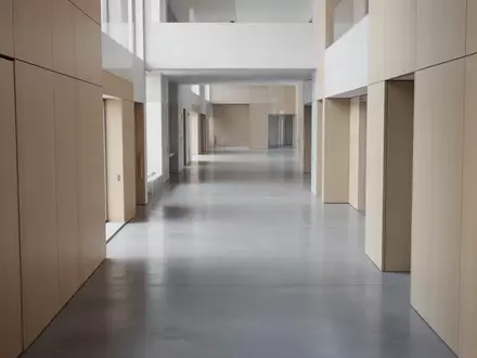 Ein minimalistischer, leerer Flur in einem modernen Verwaltungsgebäude mit klaren architektonischen Linien und Tageslicht. - Foto: über boerse-global.de