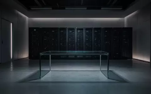 Ein minimalistisches, dunkles Büro mit leeren Schreibtischen und Server-Racks im Hintergrund. - Foto: über boerse-global.de