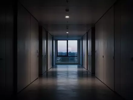 Ein leerer, minimalistisch gestalteter Büroflur im Dämmerlicht, der eine Atmosphäre von Isolation und struktureller Strenge vermittelt. - Foto: über boerse-global.de