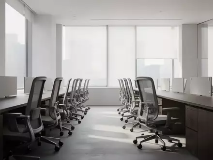 Ein minimalistisches, modernes Büro mit leeren ergonomischen Stühlen und dunklen Holztischen in einem hellen Raum. - Foto: über boerse-global.de