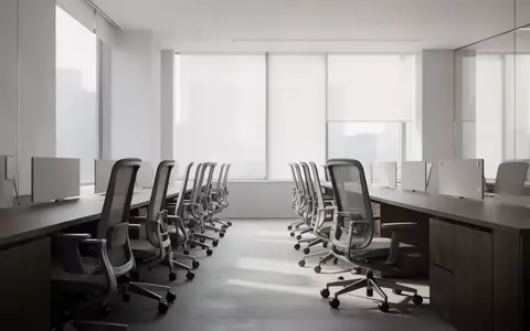 Ein minimalistisches, modernes Büro mit leeren ergonomischen Stühlen und dunklen Holztischen in einem hellen Raum. - Foto: über boerse-global.de