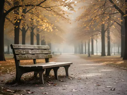 Eine leere Parkbank auf einem von goldenen Herbstblättern gesäumten Weg im Park. - Foto: über boerse-global.de