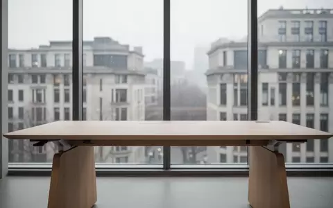Ein minimalistischer, leerer Schreibtisch aus hellem Holz vor einem großen Fenster mit Blick auf eine Stadtlandschaft. - Foto: über boerse-global.de