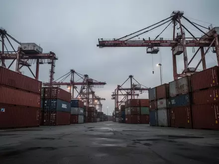 Ein stiller Industriehafen mit leeren Containern und Kränen unter einem bewölkten Himmel, der die wirtschaftliche Belastung symbolisiert. - Foto: über boerse-global.de