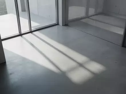 Ein minimalistischer, moderner Innenraum mit sanftem Tageslicht, das geometrische Schatten auf einen glatten Betonboden wirft. - Foto: über boerse-global.de