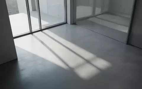 Ein minimalistischer, moderner Innenraum mit sanftem Tageslicht, das geometrische Schatten auf einen glatten Betonboden wirft. - Foto: über boerse-global.de