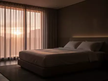 Ein minimalistisch eingerichtetes, ruhiges Schlafzimmer bei Tagesanbruch mit unbenutztem, ordentlich gemachtem Bett. - Foto: über boerse-global.de