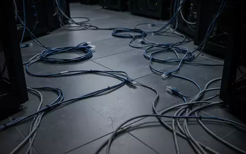 Dunkler, minimalistischer Serverraum mit verhedderten Netzwerkkabeln auf dem Boden, in bläulichen und grauen Farbtönen. - Foto: über boerse-global.de