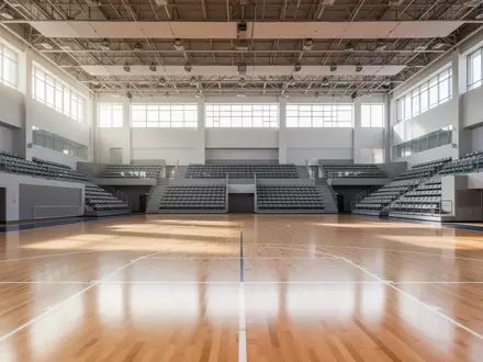 Eine leere, moderne Sporthalle mit hellem Holzboden und Tribünen bei natürlichem Tageslicht. - Foto: über boerse-global.de