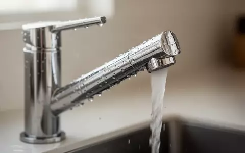 Ein moderner Wasserhahn aus Edelstahl in einer minimalistischen Küche mit Wassertropfen auf der Oberfläche. - Foto: über boerse-global.de