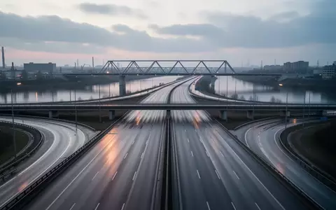 Eine leere Autobahnkreuzung bei Dämmerung mit einer Stahlbrücke über einem Fluss in einer urbanen Industrielandschaft. - Foto: über boerse-global.de