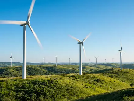 Moderne Windkraftanlage in einer sonnigen grünen Landschaft unter blauem Himmel. - Foto: über boerse-global.de