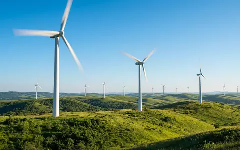 Moderne Windkraftanlage in einer sonnigen grünen Landschaft unter blauem Himmel. - Foto: über boerse-global.de