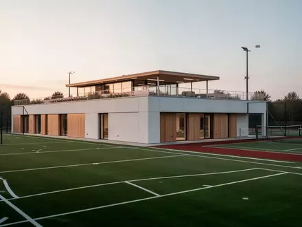 Modernes Sportgebäude mit Dachterrasse und angrenzenden Sportplätzen bei Dämmerung. - Foto: über boerse-global.de
