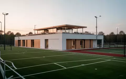 Modernes Sportgebäude mit Dachterrasse und angrenzenden Sportplätzen bei Dämmerung. - Foto: über boerse-global.de