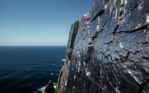 Eine zerklüftete Felsküste aus Titan mit Blick auf das tiefe, blaue Meer unter klarem Himmel. - Foto: über boerse-global.de