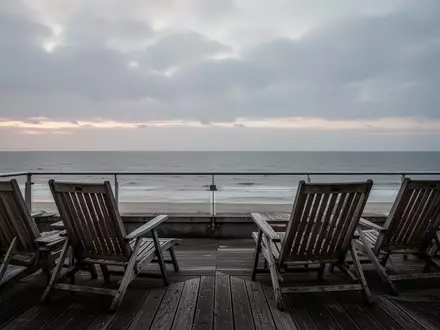 Leere Hotelterrasse mit Blick auf die Nordsee bei Dämmerung unter bewölktem Himmel. - Foto: über boerse-global.de