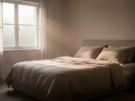 Ein minimalistisch eingerichtetes Schlafzimmer am frühen Morgen, in dem sanftes Tageslicht auf ein gemachtes Bett fällt. - Foto: über boerse-global.de