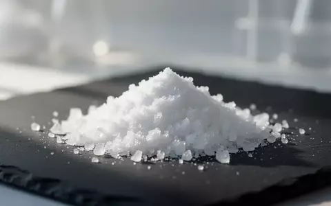 Nahaufnahme einer weißen kristallinen Substanz auf einer dunklen Schieferplatte in einer Laborumgebung. - Foto: über boerse-global.de