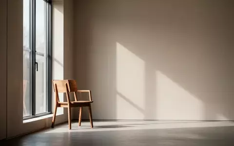 Ein minimalistischer, ruhiger Raum mit einem einzelnen Holzstuhl vor einem Fenster, der eine Atmosphäre von Stille und Unterstützung ausstrahlt. - Foto: über boerse-global.de