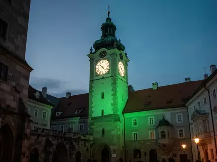 Der in grünes Licht getauchte Grazer Uhrturm bei Dämmerung als Symbol für psychische Gesundheit. - Foto: über boerse-global.de