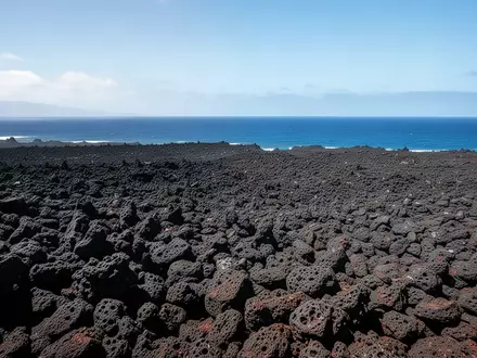 Weite, zerklüftete schwarze Lavalandschaften auf Big Island unter strahlender Sonne mit dem Pazifik im Hintergrund. - Foto: über boerse-global.de