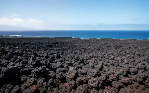Weite, zerklüftete schwarze Lavalandschaften auf Big Island unter strahlender Sonne mit dem Pazifik im Hintergrund. - Foto: über boerse-global.de