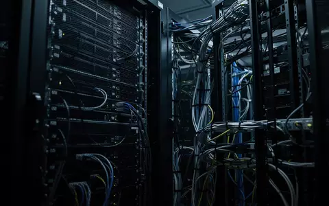 Dunkler Serverraum mit metallischen Rack-Schränken und komplexer Kabelführung in einem industriellen Umfeld. - Foto: über boerse-global.de