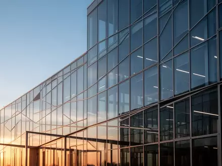 Moderne Glasfassade eines Bürogebäudes bei Sonnenuntergang als Symbol für Transparenz und staatliche Regulierung. - Foto: über boerse-global.de
