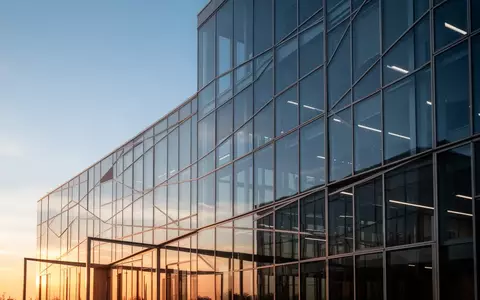 Moderne Glasfassade eines Bürogebäudes bei Sonnenuntergang als Symbol für Transparenz und staatliche Regulierung. - Foto: über boerse-global.de
