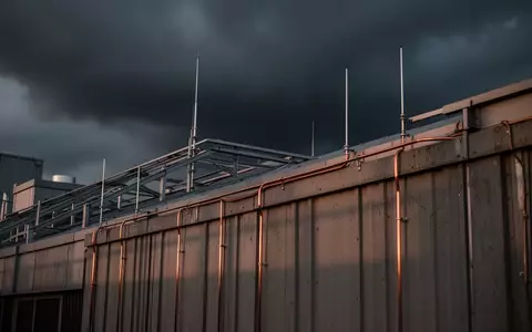 Metallische Blitzschutzvorrichtungen und Erdungsleitungen auf dem Dach eines modernen Industriegebäudes bei bewölktem Himmel. - Foto: über boerse-global.de