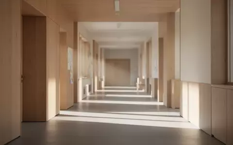Ein ruhiger, sonnendurchfluteter Flur in einer modernen Bildungseinrichtung mit minimalistischen Holzoberflächen. - Foto: über boerse-global.de