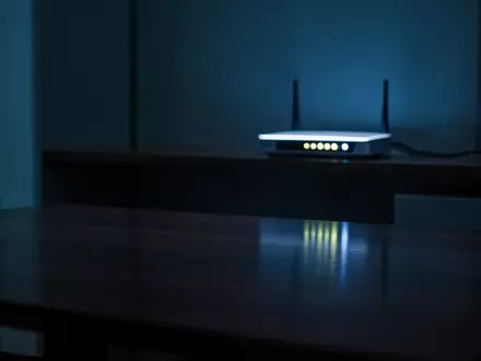 Ein schummrig beleuchteter, moderner Büroraum bei Nacht mit kühlem Licht und einem einzelnen, leuchtenden Netzwerk-Router. - Foto: über boerse-global.de