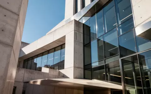 Moderne Architektur eines öffentlichen Gebäudes mit klaren geometrischen Linien und einer Glasfassade im Sonnenlicht. - Foto: über boerse-global.de