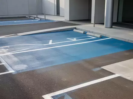 Parkplatz mit blauer Markierung für barrierefreie Zugänge vor einem modernen Gebäude. - Foto: über boerse-global.de
