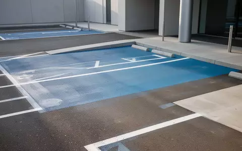 Parkplatz mit blauer Markierung für barrierefreie Zugänge vor einem modernen Gebäude. - Foto: über boerse-global.de