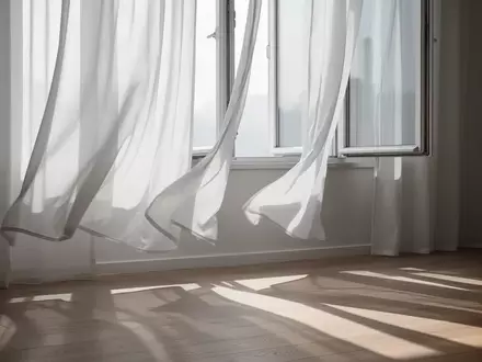 Sanft im Wind wehende, halbtransparente weiße Vorhänge vor einem offenen Fenster in einem hellen, ruhigen Raum. - Foto: über boerse-global.de