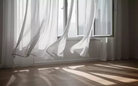 Sanft im Wind wehende, halbtransparente weiße Vorhänge vor einem offenen Fenster in einem hellen, ruhigen Raum. - Foto: über boerse-global.de
