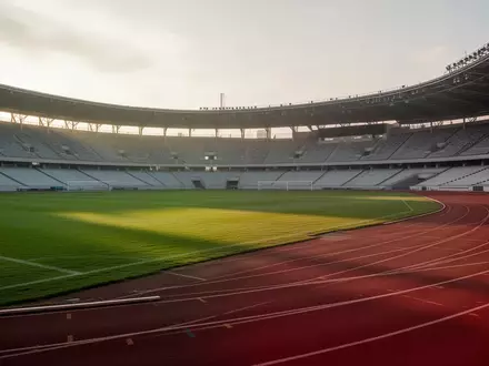 Ein leeres, professionelles Sportstadion mit einer grünen Rasenfläche und einer Laufbahn bei natürlichem Morgenlicht. - Foto: über boerse-global.de