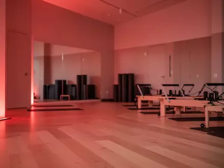 Ein minimalistisch gestalteter Yoga- und Pilates-Raum, der in ein sanftes, warmes rotes Licht getaucht ist und eine AtmosphĂ€re der Regeneration vermittelt. - Foto: ĂŒber boerse-global.de