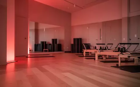 Ein minimalistisch gestalteter Yoga- und Pilates-Raum, der in ein sanftes, warmes rotes Licht getaucht ist und eine Atmosphäre der Regeneration vermittelt. - Foto: über boerse-global.de
