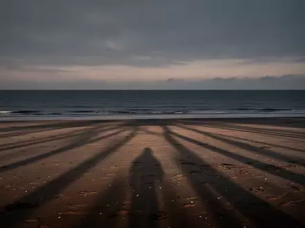 Ein einsamer, leerer Strand bei Dämmerung mit langen Schatten auf dem Sand und Blick auf das ruhige Meer. - Foto: über boerse-global.de